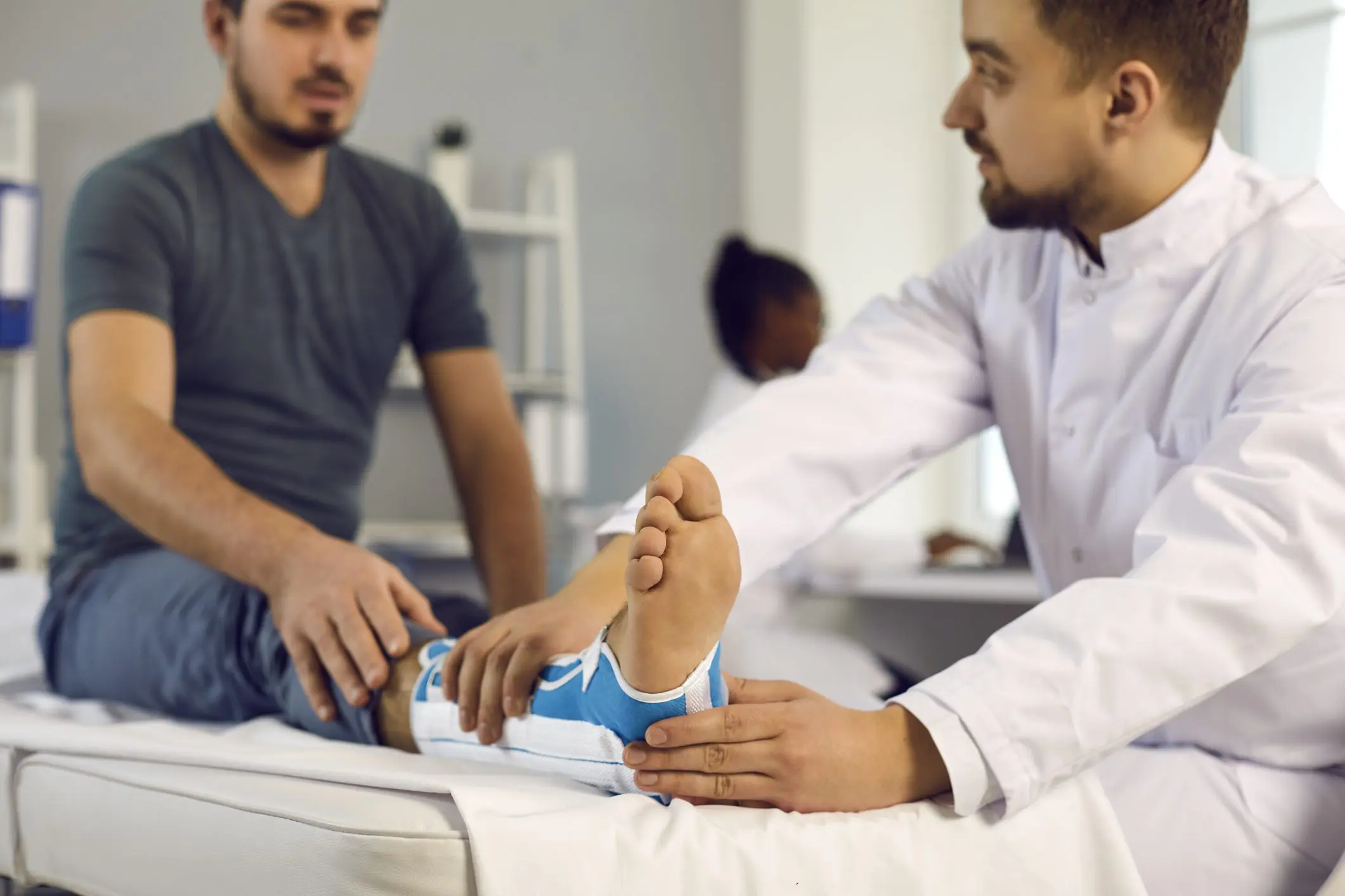 Ankle injury bone fracture, emergency first aid splint, medicine and healthcare. Doctor examine patient with broken leg trauma orthopedic bandage lying on hospital bed. Focus on foot in care bandage