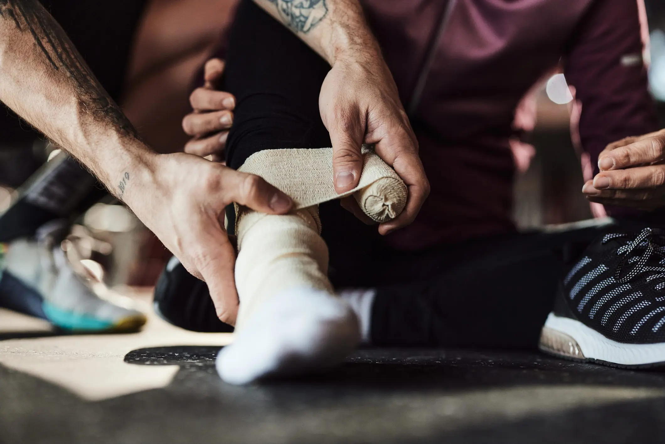 Close up of unrecognizable coach bandaging injured athlete's ankle in a gym.